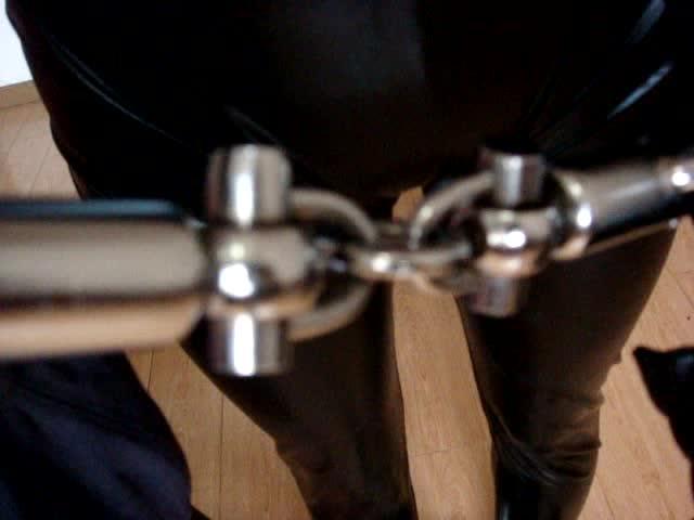 Catsuit Girl in Bound ©Leather Play<br><br>Featuring: metal bondage, chain, catsuit, blindfolded, chain, crotch rope, hogtie, breast bondage, and ball gagging