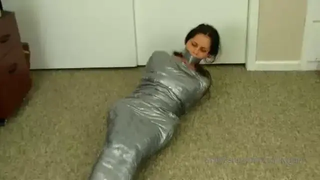 The Mummification Of Cali Logan You scamper around looking at Cali Logan’s desk when she catches you! “What are you doing?!” Without hesitation, and no explanation, you fully take over and dominate Cali Logan. Within just a blink, Cali is covered head to toe in duct tape bondage. You completely mummified Cali! You gave Cali a full body silver duct tape straight jacket track suit and just watch Cali roll around like a little silver caterpillar.    Cali moans through her ball gag AND duct tape gag. She can’t move a single limb either.
