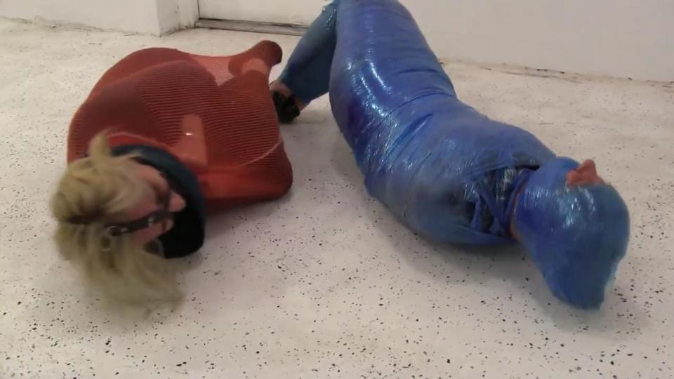 Vivienne & Fayth Scientifically Cocooned Professor Vivienne & I meet up at the secret testing facility to discuss our life saving landmine inventions. I insist mine will win the government contact and she insists hers is the better.  Little does Vivienne know is I have one in place in the floor and as her and I talk smack she steps on it and BAM, she lands into my invention as she is squeezed into a ball and stuck inside a breathable but unforgiving cocoon.  She barely can struggle around as all that is sticking out of the cocoon is her blond hair and pretty face.  I then examine my invention as i watch in my lab coat and high heals how she is helpless inside. Vivienne protests and insist I let her go but this is the test i needed as this is the 1st time its being tested on a human.  It is working splendidly.  She is unable to use her hands, feet, and rolling is very difficult.  I then realize she set her invention up as a trap as well, as it goes BOOM and I am instantly entrapped inside her landmine cocoon. I am tightly inside many many layers of plastic. I instantly protest and squirm the best I can.  Her and I struggle all we can bickering and bitching at each other for doing this to the other. We still both insist that we are going to win the contract but little do we realize that there is no escaping the cocoon until help arrives. We are both too bitter and mean to each other to think about that right now. I eventually realize I have a secret remote and I activate it and BOOM...Professor Vivienne is instantly gagged tightly and efficiently with a leather strap panel ballgag head harness. Ha.  I cant stop giggling at her and talking more smack to her knowing she is so screwed now. Minutes later, i see Vivienne reaching for something inside her cocoon but i don’t know what until BAM...my head is instantly wrapped tightly with several layers of this inescapable cocooning material.  All that you can see is my eyes and my nose so I can breath. She then bickers from behind her gag.  We both are frustrated and struggling violently against each other.  We both know we are stuck until help comes and both of our cocoon inventions are great.  I just sure hope we can learn something from each others scientific inventions.<br><span style='color:#b0b0b0;'>[隐藏文字，购买后可见]</span>