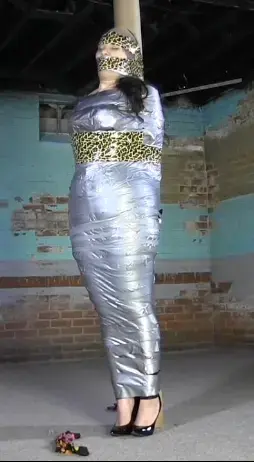 Tied up, mummified and gagged 3 times 红色系在灯杆上，穿着闪亮的裤子、紧身胸衣和蕾丝衬衫。她穿着一件差不多3英寸的黑色球衣。她看起来很简单。我给她加了一根裤裆绳，然后我开始用胶带把她的腹部包起来，在她的[不可描述]上加了3个衣夹，然后用薄胶带把她的胸部包起来，因为她流了一身口水。然后她嘴里塞着及膝高的袜子，头上缠着胶带到柱子上，我在她的胸部和腿上再加上胶带。我取下那个塞子，把一条大缎子内裤放进她的嘴里，用透明胶带缠在她的头上，然后用透明胶带缠在她的[不可描述]上，然后再用胶带再缠上去。她的嘴被脱了下来，另一条内裤塞进了她的嘴里，一顶丝袜盖在她的头上，然后用胶带粘在上面，没有把她和电线杆连接起来。她把头转来转去。我把豹纹胶带粘在她身上，然后把它包在她的头和杆子上。当磁带发出吱吱嘎吱的声音时，她专注于呼吸。最后我去掉了插科打诨，拍到了她从柱子上松开的镜头。Red is tied to the pole in shiny pants, corset and lace shirt. She is wearing a black ballgag that is almost 3 inches. She makes it look easy. I add a crotch rope to her, then I start taping her up at the midsection and add 3 clothes pins to her nipples and then take thin tape and tape up her boobs as she drools all over herself. Then she gets knee high socks in her mouth and duct tape wrapped around her head to the pole and I add more tape above her boobs and down her legs. I remove that gag and put a big pair of satin panties in her mouth and wrap clear tape around her head, then clear tape over her breast bondage before going back over it with duct tape. Her gag is taken off and another pair of panties shoved in her mouth, a stocking cap over her head and then duct tape over that, not connecting her to the pole. She is moving her head all around. I add leopard tape to her body and then wrap that around her head and the pole. She concentrates on breathing as the tape makes nice little crunchy noises. Finally I remove the gag and get a shot of her coming undone from the post.<span style='color:#b0b0b0;'>[隐藏文字，购买后可见]</span>