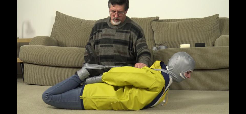 205 - Jeanette - Triple Gagged and Hogtaped Jeanette has really begun to enjoy bondage, and so she decides she needs to take the triple layer gag challenge!  Wearing her favorite raincoat, jeans, boots and turtleneck, she’s bound to a chair in preparation for the start of the challenge.  First, her mouth is stuffed with socks and her entire head wrapped in elastic bandage until only her eyes are free.  Next, sticky grey duct tape covers all of that!  Finally, her turtle neck is pulled up over her mouth and taped in place!  She tests the gag, repeating the phrases I give her and “mmpppphhh” through her packed mouth.  Satisfied that she can’t call for help, it’s time for the next challenge:  A nice, tight, taped hogtie!  But since she’s a struggler, she gets something extra!  Her hands are wrapped in tape, transforming them into useless mitts.  The tape is wrapped around her feet and head, forcing her head back!  She’s never felt anything like that and quickly realizes she’s in trouble!  Just to make SURE she won’t get out, I add a bit of hope to the hogtie and leave her to suffer! <span style='color:#b0b0b0;'>[隐藏文字，购买后可见]</span>