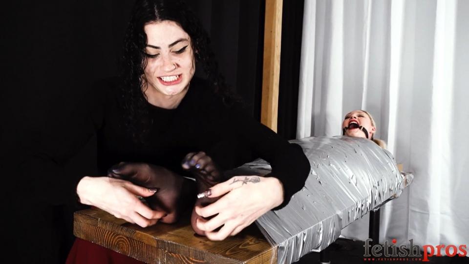 Arielle Aquinas In a Duct Tape Cocoon Under Lydia Black Wow, this is an especially wild one! Arielle Aquinas is bound to a wooden table, completely restrained by a cocoon of gray duct tape across every inch of her body except for her nylon feet, face, and blonde head. Then Lydia Black adds to the constrictive fun by putting in an open-mouth gag and further securing Arielle’s head to the table with cellophane and the remaining duct tape. Then Lydia’s devilish mischief really begins, tickling, sniffing, and licking Arielle’s helpless feet, setting off gales of laughter. Lydia drags her nails across the cocoon, then drips her saliva into Arielle’s open mouth. What a recipe for mayhem! Arielle is sweating under the tape, utterly immobilized as Lydia sits on her, grinding her pussy against her, squishing Arielle’s tits through the cocoon too and tickling her feet some more. And as Arielle is used like this, she keeps telling Lydia “thank you” as the raven-tressed vixen rides her restrained friend’s body to orgasm!<br><span style='color:#b0b0b0;'>[隐藏文字，购买后可见]</span>