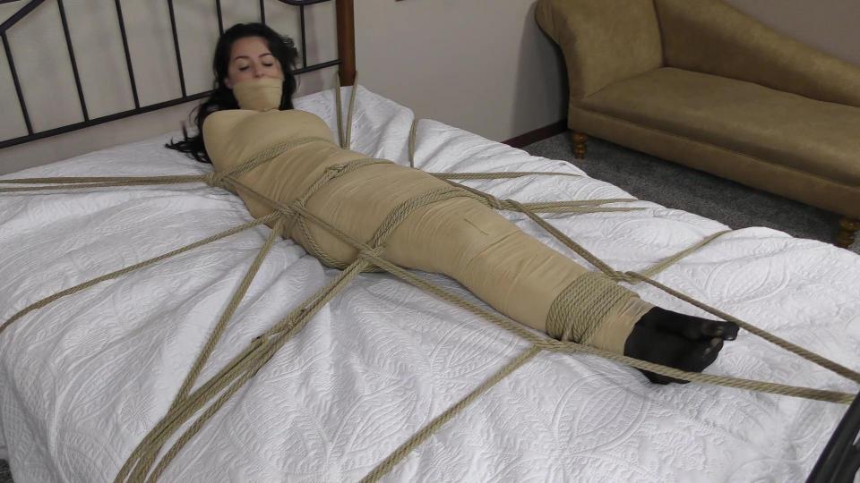 QT0911 Kristen Moore (is-qt-km043) Kristen Moore is being held for a big payday and her captor wants to make sure Kristen cannot escape. Wearing only her sexy black lingerie with her hands tied behind her back, Kristen is wrapped tightly from her shoulders to her toes in tan vet wrap. She is then tied down to the bed in a web of rope! Despite her predicament, Kristen is confident she can escape and continues to sass her captor until she is gagged with a thick layer of more vet wrap. Deprived of her voice, Kristen energetically struggles against her bindings, determined not to give up! 