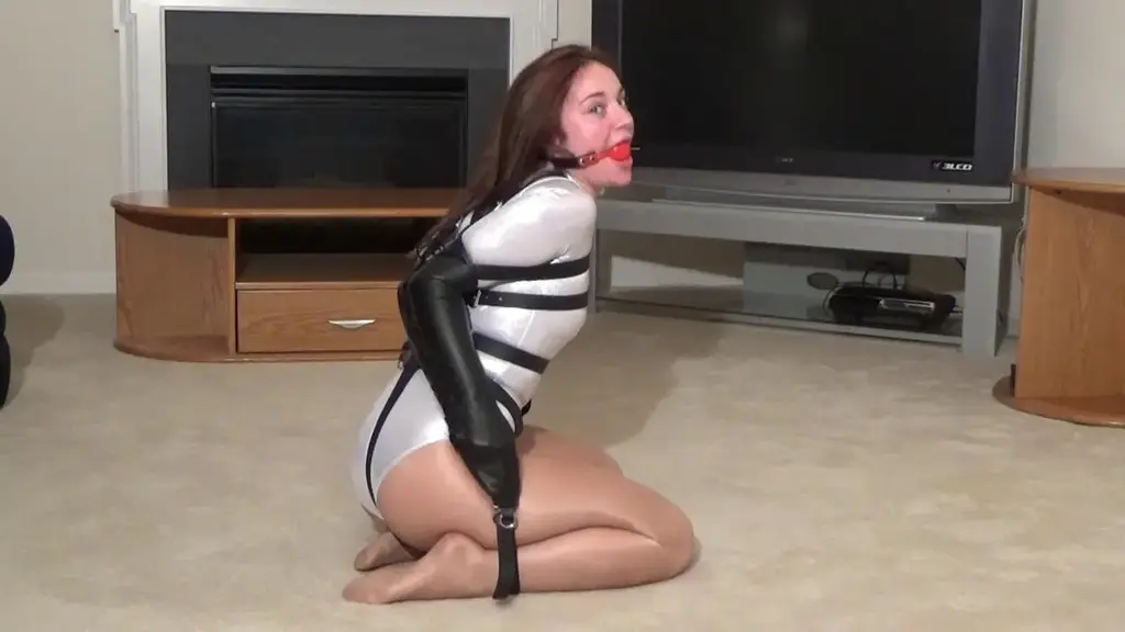Khloe Leotard &amp; Leather Restraints This gorgeous brunette shows off her assets and flexibility in this video. Khloe wears a shiny silver spandex leotard that hugs her curves with shiny pantyhose tights as her arms are tightly bound together in the leather armbinder behind her back. She has a leather body harness strapped in as well and the ballgag makes sure she can't complain too much as our assistant helps during the video. Khloe gets her legs bound separately with leather bondage restraints making this challenge a bit more difficult. She keeps crying " I want ice cream"! We agreed that if she can escape on her own that we'll get her whatever ice cream she wants. Khloe really tries to escape as she struggles, wiggling her arm and even trying to go for the straps around her legs but it's futile. She makes the greatest facial expressions and those eyes sparkle as she does lots of gag talking begging for help and even allowing us to give her some spanks if we let her out. When it didn't appear she was struggling for real, her reaction was "I am really trying, please help me"! This girl belongs in tight bondage. 