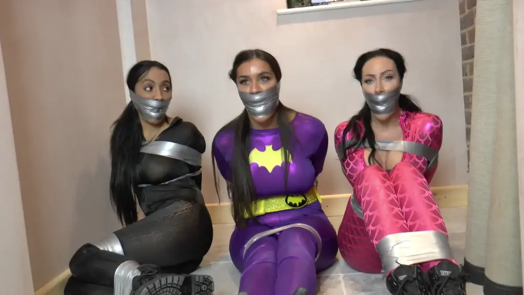 Scarlett, Mila &amp; Courtney in: Tightly &amp; Kickin' - Beyond the SteamRoom &amp; Concealed  Complete title:<br><br>Scarlett, Mila & Courtney in: Tightly & Kickin' - Beyond the SteamRoom & Concealed Within the AnteChamber of Awe! (Extra Tape Slapped Cut) (HD)<br><br><br>Our Story: Our comely crime fighter, in full costume, chatting excitedly over the telephone to what sounds like Batman. She needs no help on this one, so refuses to tell him where the lair is. This is going to be HER success and she won’t rest until the Combat Squad are mouldering behind bars and the legendary Duck’s Head stays exactly where he belongs – in the far, far away galaxy to which he has been banished… Too much genre blending? Oh well, you probably came here for something other than credible plots, hmmmm? Yes, we thought as much…<br><br>Spirited Miss BatGirl is adamant – she requires no assistance form her fellow crime-battler, and that is only her FIRST mistake! Heading off to have a snoop around the old Duck’s Head manse, she overhears the Combat Squad plotting, and, she being BatGirl, blunders straight into taking them on. Of course, they have something magical, and of course, the beauty is turned to mind-bent jelly, and of COURSE, she is bundled away by the Hench, Jenkins, who binds and gags her in the old Steam Room and stalks off to await further instruction… But, can we trust this chap… Hmmmm…<br><br>Meanwhile, Batgirl, heavily bound up, with a red bandana tied very tightly over her mouth, struggles valiantly! Now, with BatGirl helplessly bound and gagged in the Steam Room, all could not be going more perfectly for the villains of this piece. Those busty Combat Squad chicks ensure the final co-ordinates are entered into the Cyclone System and the collision sequence of stars shall result in the return of the arch-evil One, Duck’s Head!<br><br>Using his enchanted cane to overcome that bratty little bat-chick, their chief Hench has roped her up real good and turned up the HEAT… But, what if BatGirl can escape her peril? Can she stop them all before they complete their mission? What do YOU think…?<br><br>We now keenly feature a super-hot cleave and lotus-truss for BatGirl, who eventually gets loose, confronts and does battle with the Combat Squad, only to be overpowered by Jenkins. Preview - Turns out later that Jenkins is a traitor (surprise surprise) and has bound and gagged the Combat Squad babes!!! Now, they squirm tightly hogtied and gagged in their bedroom and are quite the sight for the lovely BatGirl, who naturally is too busy mocking them to notice a persuader being levelled at her. Hands up… BatGirl!<br><br>Now, the three lovelies, all in the same boat embark upon a truly epic wrapped and WRAPPED struggle session concealed with the AnteChamber of Awe. This looks like a lot fun, right? Enjoy…