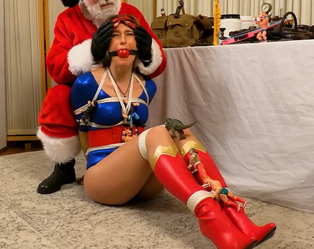 Super Kaan Vs Evil Santa - Ophelia Kaan As this fantasy from Skyryder23 begins, The international criminal known as Evil Santa is working in his evil workshop at the South Pole in preparation for the holidays when Super Kaan bursts into his lair and confronts him. The champion of justice confidently announces shes catching him early so he cant pull of one of his nefarious schemes during the true holiday season. The festive villain chuckles and commends the masked adventuress for a nice try, and then activates a special switch. Much to her surprise, Super Kaan is then attacked by Evil Santas wicked creations -- and the masked crimebuster is powerless to resist the dark magic which gives them life! The sinister toys bind her with enchanted rope and shes powerless to stop them when they ballgag her (shown on-screen). Once Super Kaan is subdued, her nemesis taunts her as he removes her mask, and then he snatches the magic amulet that grants the booted babe her amazing abilities. He ridicules her for falling into his trap, and mocks her hubris for bursting in without a plan. He then promises his trussed-up guest that he has some wonderful things planned for her, and he leaves her alone to make his depraved preparations. Super Kaan struggles against the snug ropes, but without her amulet she has no hope for escape! She squirms against her bondage, unable to reach the knots, and unable to pick them loose with her gloved fingers which she can. Then Super Kaan is hogtied. She moans and helplessly rolls around on the floor of the workshop, knowing shes completely at the mercy of her cruel host. What does Evil Santa have in store for her next?<br>当《Skyryder23》的奇幻故事开始时，被称为“邪恶圣诞老人”的国际罪犯正在他位于南极的邪恶工作室里工作，为假期做准备，这时超级卡恩闯入了他的巢穴并与他对峙。这位正义的捍卫者自信地宣布，她要提前抓住他，这样他就不会在真正的假期里实施他的邪恶计划。欢乐的反派咯咯地笑着，称赞蒙面女冒险家的好尝试，然后启动了一个特殊的开关。令她惊讶的是，超级卡恩遭到了邪恶圣诞老人邪恶造物的攻击——蒙面的犯罪终结者无力抵抗赋予他们生命的黑魔法！邪恶的玩具用魔法绳子把她绑起来，当他们把她绑起来时，她无力阻止他们（如屏幕所示）。一旦超级卡恩被制服，她的敌人嘲笑她，摘下她的面具，然后他抢走了神奇的护身符，赋予她神奇的能力。他嘲笑她掉进了他的陷阱，嘲笑她没有计划就突然闯进来的傲慢。然后他承诺他的客人，他有一些美妙的事情为她计划，他离开她独自做他堕落的准备。超级卡恩斗争与舒适的绳索，但没有她的护身符，她没有希望逃跑！她扭动着反抗她的束缚，无法到达结，也无法用她戴着手套的手指把它们弄松。然后超级卡恩被绑住了。她呻吟着，无助地在车间的地板上打滚，知道她完全被她残忍的主人所摆布。邪恶的圣诞老人会为她准备什么呢？