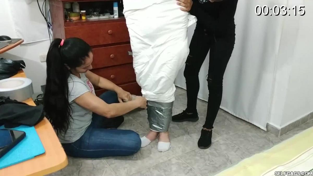 Laura, Katherine &amp; Maria in: Katherine Martinez Collared And Pantyhose Hooded In Multilayered Mu As the scene opens, Katherine Martinez is carried into the room by Maria and Laura. She is made to stand on the floor where she is wrapped in white sheets. Silver duct tape is wrapped from her ankles all the way up to her shoulders, completely covering her whole body and the sheets wrapped around it. Katherine's feet are also wrapped up and encased in duct tape!<br><br>A thong is stuffed inside Katherine's mouth and she gets tape gagged with duct tape wrapped around her head! Maria and Laura put mummified Katherine inside a napping bag and zips it. She is once again made to stand, this time on her mummified feet and with extra support from Maria so she won't tip. Silver duct tape is wrapped around the napping bag from Katherine's ankles all the way up to her shoulders to completely cover it up!<br><br>Once Katherine's multilayered mummification process is done, she gets a pair of pantyhose dragged down over her head and a posture collar locked around her neck. Duct tape is then wrapped over her already gagged mouth and her eyes to blindfold her from the outside of her pantyhose hood!<br><br>Katherine is lifted to the bed where she is made to lay. Laura and Maria laugh at her, they tease her and they humiliate her, giving each other high-fives and joking. Katherine is unable to talk, see and move. She is stuck. Trapped inside her uncomfortable multilayered cocoon!<br><br>Included in this clip: mummification bondage, duct tape fetish, pantyhose hooded, tape gagged, mouth stuffed gag, double domination, pantygag, multilayered mummification, tape bondage, collared bdsm slave, latinas, humiliation, tapegag, domination, duct tape encasement fetish, blindfolded, bdsm, gag fetish
