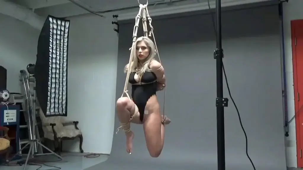 Rosie Lingerie Bound Combo Lovely blonde Rosie figured it was just another kinky photo shoot where the photographer was looking to practice his rope bondage skills. She wears a satin one piece lingerie bodysuit and has herself semi suspended with her arms tied to a pole. Everything seems to be going well until she's ballgagged and then surprisingly set up to test out how good she is at escaping. Rosie protests, talking through the gag to be let go and demands to be untied. She struggles on one foot, maintaining her balance unable to reach any of the knots.