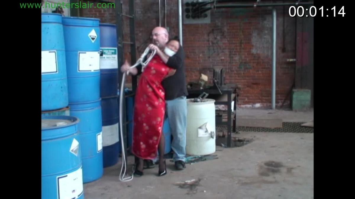 Asian captive held hostage Sexy club owner Kim Lee has been k'dnapped and hauled to an old factory hideout. She is dragged into the factory with her arms tied brutally tight behind her back, her mouth is stuffed and sealed with duct tape. She is still wearing her long silk red cheongsam dress and 6 inch stiletto heels from the club. He pushes her back against an old steel ladder and lashes her chest and shoulder tightly to the ladder. She kicks at him complaining and cursing into her gag. That only get her angry, he lashes one of her ankles to the base of the ladder and then pulls her other foot off the floor and ties it to the ladder so she can't put it back on the floor. He leaves her there like that in agony from the brutally tight ropes and being off balance on one high heel