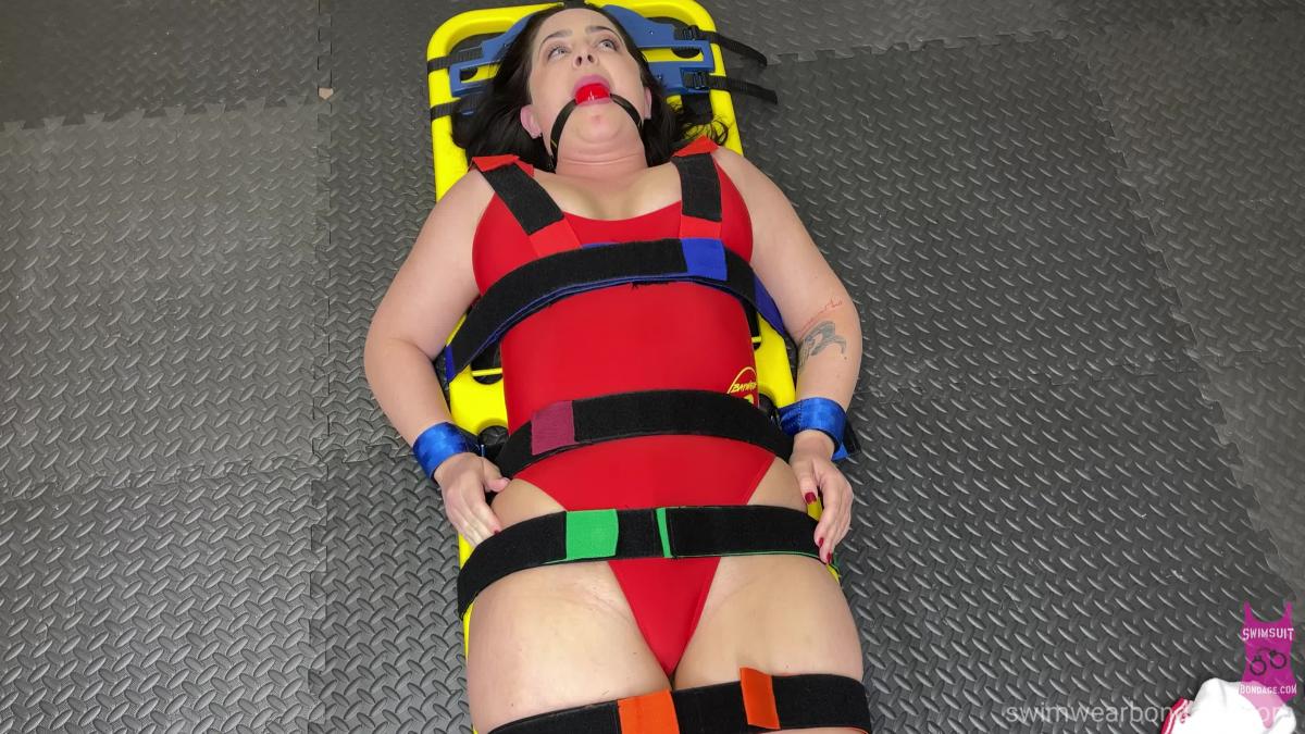 375 Tilly Lifeguard Jess Jordan gives Tilly a escape challenge with a real lifeguards backboard, only she adds some EMT wrists restraints and a red ball gag. TIll is wearing a Baywatch lifeguard one piece swimsuit uniform. 