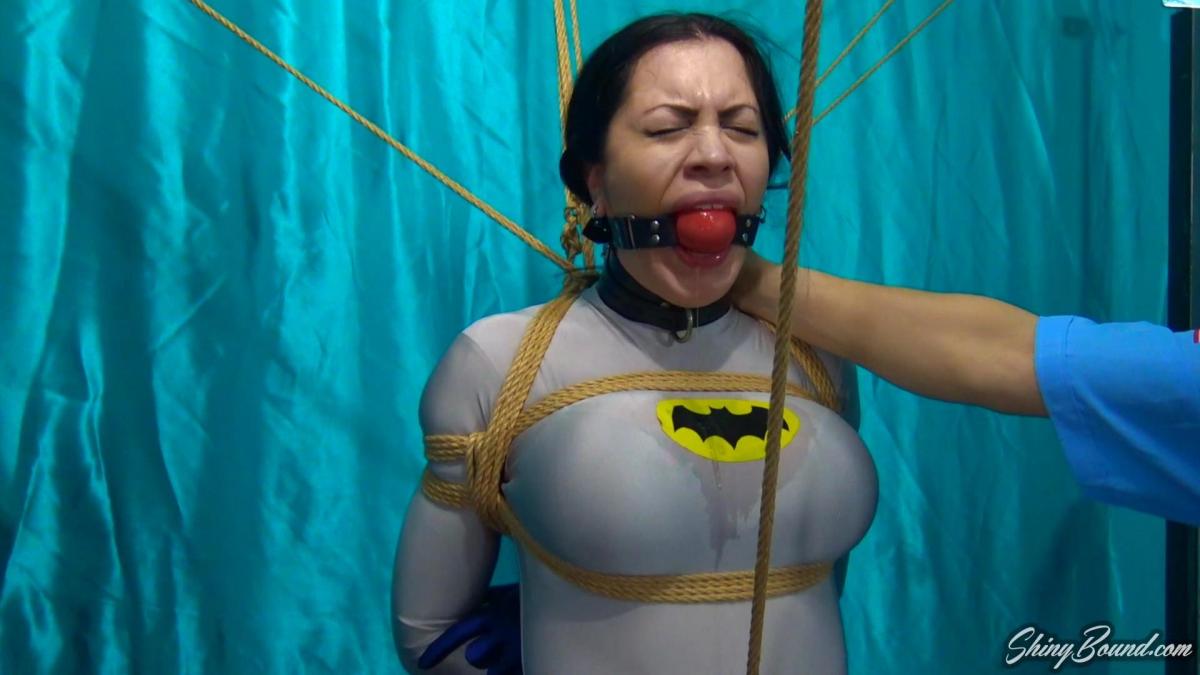 BATWOMAN LOCKED UP PART 2 Now in part 2.. Batwoman once again opens her eyes and is tightly bound.. This time she is semi-suspended up on her knee points, with her arms welded behind her and a Hitachi magic wand vibrator strapped between her thighs. Her cape and utility belt are hanging up on a post, taunting her and making her feel even more helpless. Bolton enters and begins to remove her mask. She angrily shakes her head and tries to resist. "Ah.. Cassandra Cain? Oh this is too good!" He swaps out her ball gag for a larger panel style gag and pulls the strap extra tight. "You're gonna be my little sex toy Batwoman. Let's give you a couple of orgasms to get warmed up!" He flips the switch on the vibrator. Now unmasked, Batwoman is left to her predicament, struggling and drooling all over her chest. She tries her best to wiggle free, but over time she grows weaker and weaker and eventually succumbs to the Hitachi, climaxes, and slumps over completely exhausted.