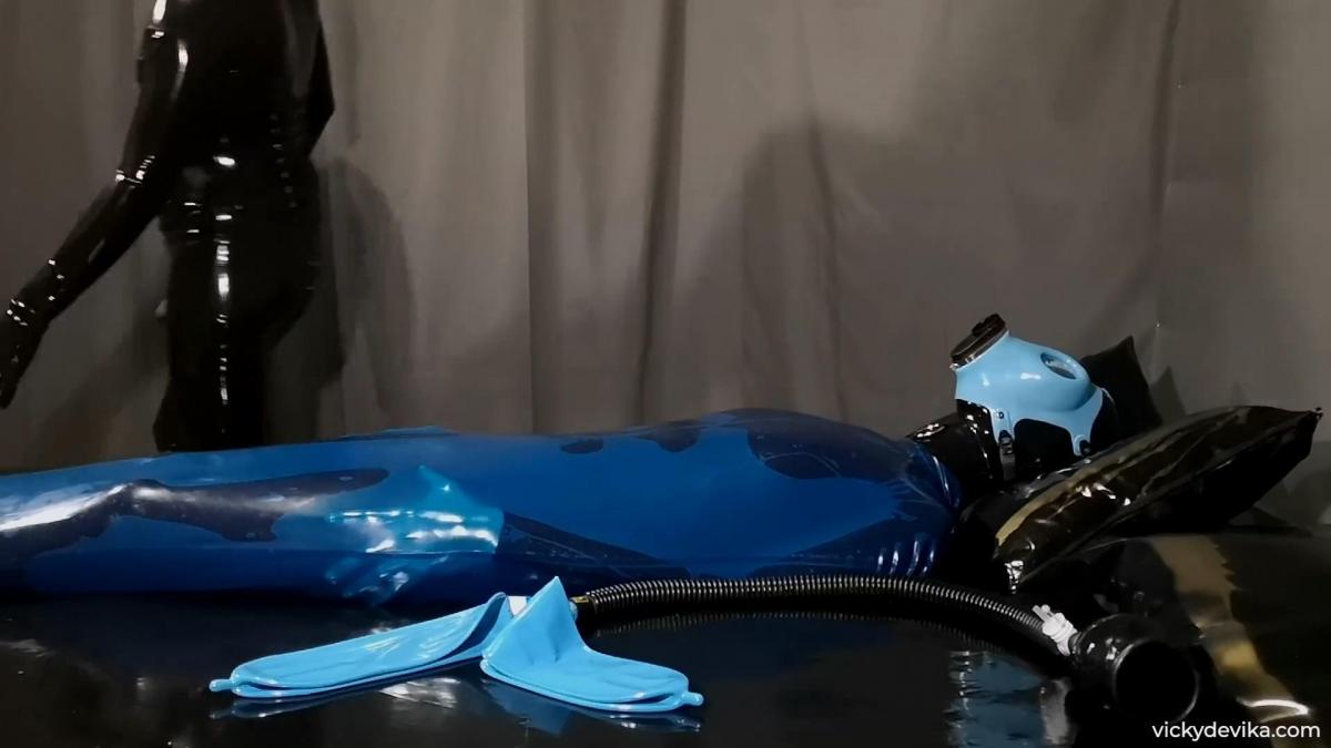 Turning Blue I'm blue, I'm in need of some bondage. Blue rest sack, blue gas mask, blue rebreather bags. With this setup I will most likely turn blue. Rest assured the process is being overseen by none other than Mistress Nina X. She waits patiently as I struggle my way into this rubber rest sack until poor me needs some assistance. She then straps the gasmask to my face and attaches the hose connected to two 3L bags. I think she enjoys playing with my air supply. She also tends to enjoy using that magic wand while I remain helpless. I lose myself completely and become one with the rubber. Isn't that just pure bliss?
