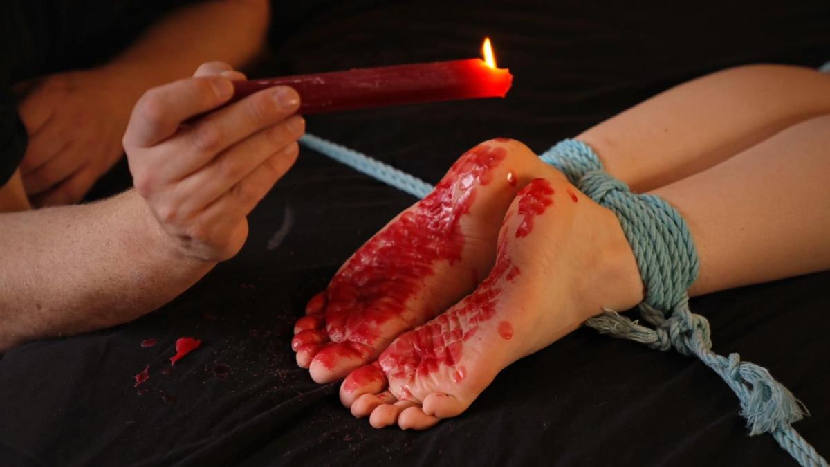 Faerie Willow's Bastinado Session Part Two: Hot Wax (VID0813B, 1080p MP4) Now that Faerie Willow's feet have been properly sensitised by the first round of bastinado, it was time to take her wrinkled soles to task for another of my favourite things - hot wax play! I tied her back down to the bed, feet at one corner for proper access. Wax is one of those strange sensations that plays out very differently from day to day. It can be almost relaxing and mild, or it can be on the edge of unendurable. What I was aiming for was surfing the edge of pleasure and pain the whole time.<br><br>I was starting to get a better read on Willow's body language and breathing after the bastinado. So I could play around a bit with the variations available - heels are usually must less bad than toes, especially if you dribble the burning hot wax in between toes or worst of all under existing wax which acts as an insulator and stops the wax cooling off so quickly. Her arches were exquisitely sensitised from the bastinado (her soles were hot even before applying the first drip of wax). She was soon moaning and squirming and almost swearing as the sensations ramped up towards overload and overwhelming.<br><br>Every time it was getting too much, I backed it down again, going back to drips on her heels. But even so her feet were soon covered completely in wax. I was far from done, though. So it was time to clean them off and start again. I wondered how she would respond to firm pressure as I slid my thumbs under the wax to dislodge it. Quite strongly, as it turned out! What would have been a mild massage sensation an hour before was transformed into an almost-unbearable re-stimulation on stinging sensitive soles! Of course, I needed a little help from a strap to clear off the last bits of wax - more bastinado to make her poor feet even more sensitive and tender!<br><br>Then it was time for a second full and complete coating of burning hot wax on every square millimetre of her delicious soft soles. The Willow I untied was altogether more subby and subdued than the bratty version who had dared me to do my worst while I was tying her up an hour before. She dutifully complied with her orders to pick the small bits of overspill wax off the carpet - still bound hand and foot.<br><br>It was time to break for lunch and regroup before the next part of her submissive session....