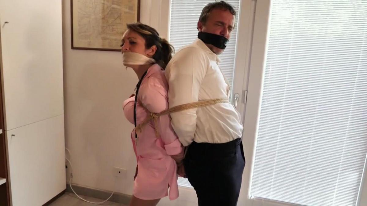 Alba &amp; Tony - Bondage Clinic Adventure MP4 1080p In a private clinic, a Doctor, Tony Houston, and a nurse Alba Zevon were there while other staffs were left as it was already after the business hours. The nurse iwas checking on the medicine stock in the storeroom while the Doctor was in the therapy room. When the nurse heard of the abnormal sound, she approached to the storeroom door, and at the same time, the robber gets into the storeroom and hreaten the nurse. <br><br>The robber asks the nurse to use a cloth to stuff her mouth and gave her another piece of white cloth for OTM gagged. The doctor try to ask the nurse to come to the therapy room but there was no response, so he try to approach to the storeroom and found the nurse was being gagged; at the same time, the robber came out and threaten the doctor to stuff a cloth into his mouth and ask him to remove his tie for OTM gagged. The robber then tied the doctor and nurse up by using rope on their wrists and ankles; and use a rope to tie them back-to-back and keep standing. Both are wearing uniform at that time. The robber leaves the storeroom, and they keep struggle and finally the rope loose and they can hop to the storeroom exit for help. At the exit, the use their lip to help each other to remove the OTM gag.  The robber back to the storeroom at that time. As a punishment and prevent them to leave again, the robber asks the nurse and doctor to remove their uniform (on screen stripping off). After the nurse removed the uniform, she was just wearing a white camisole and nude color panties and white socks with white shoes only. After the doctor stripped off his clothes, he only wearing a white camisole and white color briefs; then he ties up both Doctor and Nurse to the chair, with “a cross” on the chest; and wrists was placed behind the chair back and tied up by rope and the ankle for them were also tied up by rope. The robber uses a piece of brown/parcel color tape to gag them. The doctor and nurse just sitting on the chair side by side with mummmmph sound while the robbers keep on searching the medicine.<br><br>After struggling for a while, the Doctor first get his wrist loose and then he removed his gag, then he unties sthe nurse’s wrist and removed her gag. The nurse was so scared, and the doctor ask her to keep quiet.  They untied their ankle and try to use the cell phone on the floor to call for police. Unfortunately, the robber back to the storeroom after collected the medicine and ask them to stop.  As a punishment and prevent them to leave again, the robber asks the nurse and doctor to remove their camisole (on screen stripping off). <br><br>After the nurse removed the camisole, she was just wearing nude color bra and panties and white socks with white shoes only. The robber than use black duct tape to tie up the nurse wrists and ankles and gagged her with white cloth stuff to her mouth with a piece of black duct tape (on-screen tied up). <br><br>After the doctor stripped off his camisole, he only whites brief with black socks; the robber tied up the doctor wrist and ankle with black duct tape and gagged him like the nurse (on screen tied up). To secure them, the robbers then tied them up back-to-back and sitting on the floor. The robber then keeps searching on the cash in the clinic. The doctor and nurse keep struggle with gag talk and muuumph sound. They try to approach to the scissors on the floor inside the storeroom; and finally, they success and untie themselves again; but without removed the gag. The robber took the money and try to leave the clinic, but he saw the couple try to ask for help and stop them. For this time, the robber asks them to remove all underwear and tied up them again by sitting on the floor side by side in nude body. Their wrist and ankle are tied up by black zip tie this time. The doctor and nurse try to scream out after the robber left the clinic and hopping to the front door of the clinic but only muuumph sound and gag talk amount them. Later, due to their struggle, both fell to the floor and lying on the floor.  <br>Since the air conditioning was shut down after business hours; they were sweat... What is going to happen to them...?? (BONDAGE, BONDAGE COUPLE, NAKED BONDAGE, ROPE BONDAGE, TAPE BONDAGE, OTM, TAGE GAG, ON-SCREEN STRIPTEASE, BAREFOOT, ENGLISH DIALOGUE, ROLE PLAY, CHAIR TIE)<br><br><br><br>