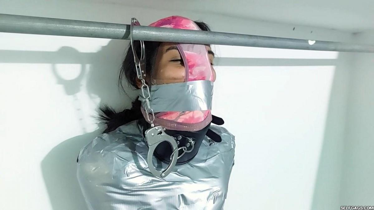 Lock Up The Panty Hooded Mummy! Wrapped up tight in strict tape mummification bondage by a couple (Laura and Jose), Maria Martinez has a posture collar locked around her neck, a thong stuffed in her mouth, and a clear tapegag wrapped around her head. The clear tape wrapgag is then covered with silver duct tape to match her restrictive bondage cocoon.<br><br>The mummified girl is put on the floor to lay and struggle as much (or little!) as her tight encasement bondage allows. The couple returns and the woman reaches up her skirt and takes off the dirty panties she's worn all day. <br><br>Maria gets panty hooded and has another layer of tape wrapped around her mouth from the outside of the panties to hold the humiliating pantyhood in place! She is then dragged into a nearby room and locked to a clothes rod with a pair of handcuffs attached to her collar.<br><br>She is teased and taunted by the couple and left to stand and inhale the fumes from the woman's dirty panties!