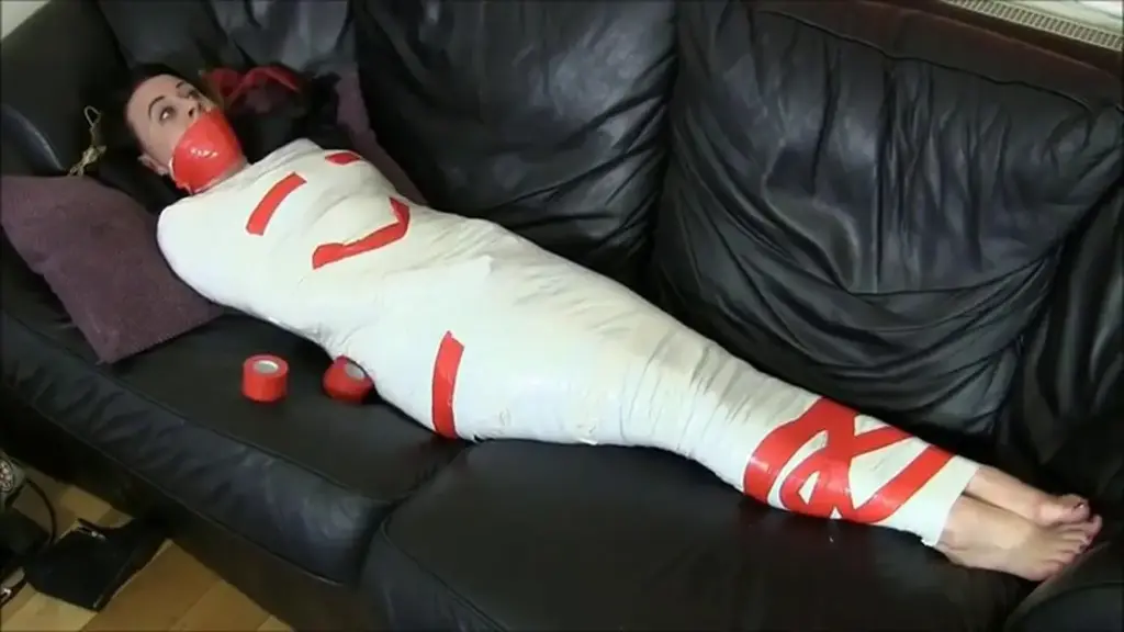 Carleyelle &amp; Jet in: Lazy Roommate: Tape Gagged &amp; Tickled In Tight Mummification Bondage!  Carleyelle & Jet in: Lazy Roommate: Tape Gagged & Tickled In Tight Mummification Bondage! <br><br>That's it! Jet Black has had enough of her lazy roommate Carleyelle lying on the couch watching tv all day while the house look like a total mess! Jet enters the living room only to find Carley enjoying herself as usual. Carley lie herself sick as an excuse for not doing the dishes but Jet doesn't buy it and demands her to hand over the remote control. Carley refuse to give Jet the controller so Jet attack her feisty roommate and dominantly wrestle her into a tight and powerful handgagging grip to shut her up! Carley is outraged for being held down with a hand over her mouth and furiously tries to escape the silencing handgag Jet puts on her. Fail! Carley doesn't manage to fight off Jet and the next thing she knows she's getting wrapped up on the couch! Jet finish her thorough tape wrapping work to fully immobilize Carley, leaving only her bare feet unwrapped! Carley angrily bitches and demand Jet to let her go right now or else but Jet doesn't give a about what her lazy roommate has to say and decides to shut that big mouth of hers for some peace and quiet! Jet crams a yellow foam sponge in Carley's bitching mouth and ruthlessly wraps it shut with several layers of tape jerked around her head! Carley is hysterical and desperately wriggles in her insanely tight and immobilizing tape cocoon while Jet goes away to find some more tape. The tight tape gag muffles Carley's persistent whining for Jet to come back and untie her while she looks down at her exposed feet! Jet comes back with a couple rolls of red tape and reinforces Carley's gag and mummified body, also making a decorative tape smiley face on Carley's chest! Jet sits down and tries to watch some tv with Carley's feet over her lap. Carley mmmppphhs in rage for being ignored and wriggles her feet for Jet to give her some attention and let her out. Jet teasingly tickles Carley's feet while watching tv and tells her to lighten up and not be so mad all the time! Carley is so ticklish and can't help but to laugh behind her gag the more Jet tickle her feet! "The more you complain the more I'll tickle you" Jet says and goes on tickling Carley's trapped feet with Carley squirming in serious laughter, wrath and humiliation! Not only did Jet win the battle for the tv remote, she also won the full control of her lazy roomie! Way to go girl!