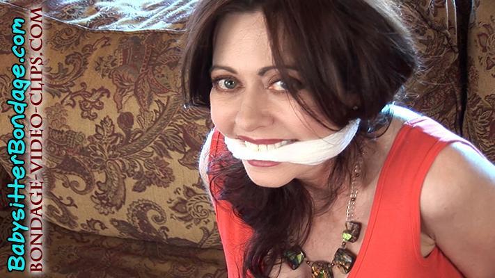 Mom Natasha Flade Pranks Her Son That a Real Robber Tied Her Up! Mom Natasha Flade Pranks Her Son That a Real Robber Tied Her Up!<br>Mom Natasha Flade’s son, Robbie, is having a sleepover and pizza party. You’re one of Robbie’s friends who has come over early for the sleepover — and with a plan for a prank! You find Robbie’s hot mom sitting on the couch, barefoot in a short, tight sundress with her cleavage in plain view (and you can’t stop staring at it!).<br><br>When Natasha tells you that Robbie is still at baseball practice and won’t be home for another half hour, you guys ask if she wants to prank her son. She’s curious and asks you you’d do that. You say you’d tie her up so that when Robbie comes home he will think she’s been bound and gagged by a real robber! Amazingly, Natasha goes along with your bondage game prank! She smiles and crosses her hands behind her back. Soon, she’s bound hand and foot, barefoot in her sundress, on the sofa. You’ve cleave gagged her, too, with a white scarf wrapped between her lips so now she can only speak in gag talk. And this mom likes to gag talk a LOT!<br><br>Then Natasha hears Robbie opening the door, so she tells you boys to run and hide quick! She plays her damsel role to the hilt, pretending to be all in a panic that a robber broke in and tied her all up! She keeps up this game for bit, but then she breaks character and starts laughing. Now all you boys come out of hiding and are laughing, too.<br><br>Natasha assumes the game is over, but Robbie decides he wants to keep his mom like this for a bit longer. He asks if he can play a ransom game since she’s already tied up, anyway. Hmm…Is mom Natasha going to go along and play more bondage games with her son and his friends?
