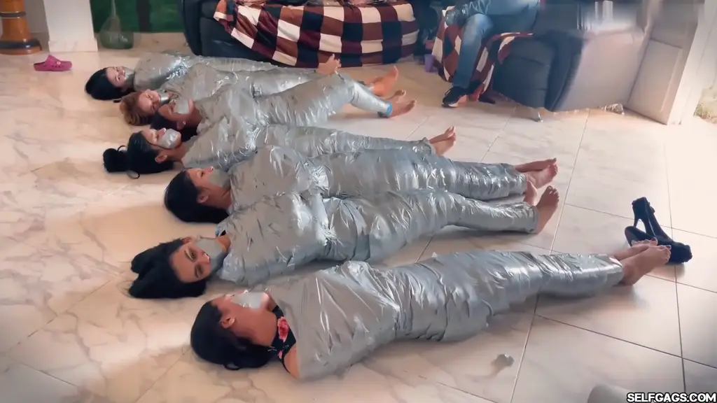 We Were All Wrapped Up and Transformed into Tightly Sealed Little Packages Seven girls find themselves completely immobilized, transformed into tightly sealed packages through intense duct tape mummification. Watch as they struggle barefoot and tape gagged, trapped in relentless tape cocoons that hold them captive. Their every move is restricted, making this a must-see for fans of intense bondage and mummification scenarios!