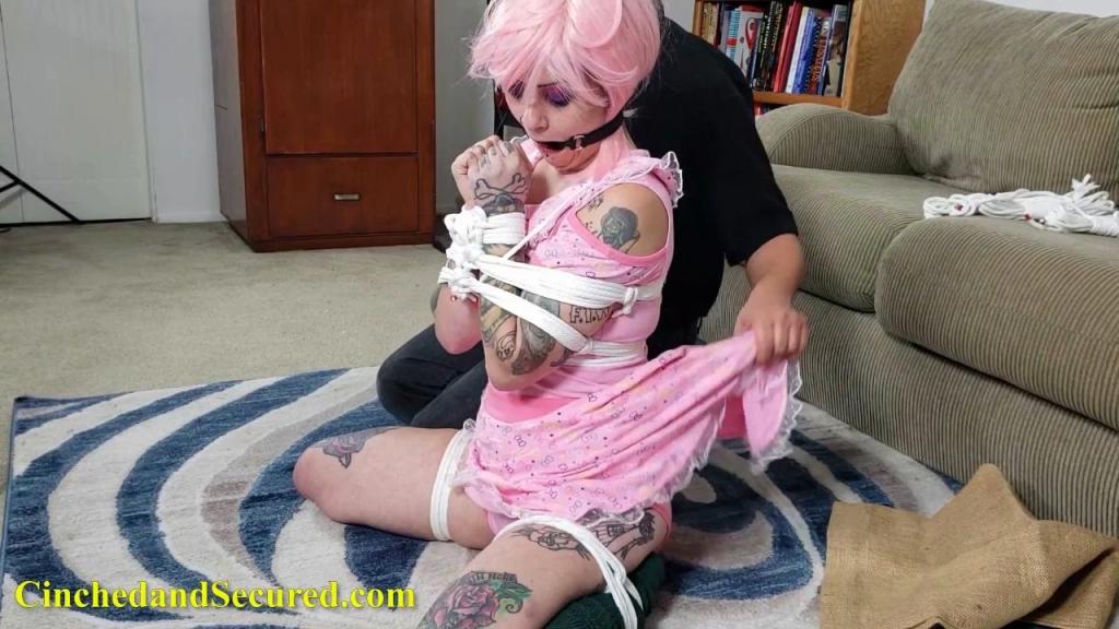 568 - The Wages of Sin - Part Four After a seemingly endless day of captivity and instruction at the hands of the demented preacher, Mallory's resistance is at it's lowest point.  She had been made to suffer through tight bondage, inverted suspensions, clamped nipples, spankings, excessive mandatory cigarette smoking and unwilling orgasm training, and now Mallory's will has finally been broken.  She'll do anything to stop the punishment and serve as a good christian girl.  Trapped in darkness, a burlap bag stretched over her head, the penitent sinner mewls in fear.  Her black goth clothing and hairstyle had been switched out for a new makeover including a childish pink one-sie and wig.  Now, she waited, frog-tied and helpless, her hands bound before her in an obscene gesture of prayer.  The preacher returned and removed the sack, revealing the ring-gagged sluts drool soaked face, and Mallory's heart sank when she was informed she'd be shipped away for further indoctrination.  Desperate to avoid torment at the hands of a new group of unknown devils, she enthusiastically agreed to become the bride of her captor.  Of course, it would not be that easy.  She'd have to prove her obedience by having a long rubber cock shoved down her throat again and again.  <br>