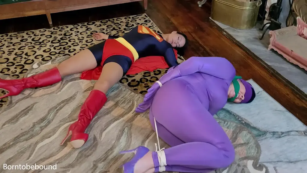 Batgirl and Supergirl in a in a bind Batgirl (Jamie Knotts) and Supergirl ( JJ Plush) split up but unfortunately for them they find themselves in big trouble. Batgirl gets all tied up in a ball and cleave gagged and soon Supergirl is caught as well. Both of them find themselves tied back to back with Supergirl very weak from the Kryptonite in the green gag. They wriggle around and eventually find themselves tipped over on their sides while blindfolded and cleave gagged. What will become of them??