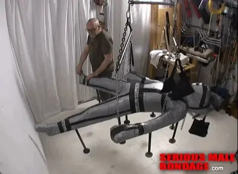 Seriously Overwhelmed <br>【乳胶男M】他带着自己的黑色乳胶连体衣，想被做成木乃伊。所以，MummyEd决定用从头到脚的托盘包装和胶带将他包裹在我们自制的“姜饼”捆绑板上。这似乎是一个相当标准的木乃伊化场景，直到我们看到头顶的悬挂。我们的起重工道尔顿能够用我们的两个曲柄绞车把他抬离地板，让他用道尔顿的攀爬旋转装置轻轻旋转。正如你所想象的，这让我们的访客QS Mud体验到了更深层次的束缚、孤立和无助感。This is a video from the archives which we shot years ago. In this scene MummyEd had a visitor by the name of QS-Mud who had brought his own black latex catsuit and hood, and wanted to be mummified. So, MummyEd decided to wrap him onto our home-made 'gingerbread' bondage board using head-to-toe pallet wrap and duct tape. This seemed like a pretty standard mummification scene until we got to the overhead suspension. Our rigger Dalton was able to lift him off the floor with our two crank winches, allowing him to gently rotate with the use of Dalton's climbing swivel. As you might imagine, this allowed our visitor QS-Mud to experience a deeper sense of bondage, isolation and helplessness.<br><br>What we didn't expect was his response once we cut him out. He seemed overwhelmed, in a good way, and it took him quite a while to come back to reality. To us, this was the sign of a successful bondage scene, which he later agreed. He had been mummified for a couple of hours. For many people, experiencing extreme helplessness and inescapable bondage can provide a way to disconnect from the world, especially if you're wearing full coverage rubber like QS was. The rubber seems to have a calming and swaddling effect, especially if you're wearing a close-fitting rubber hood. This combination of gear provided QS-Mud with a wonderful experience, exceeding his expectations. As a result, he became another happy customer at the SeriousBondage Institute!