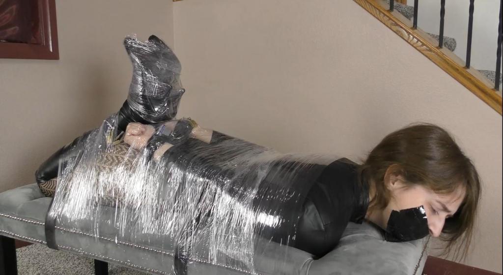 QT1411 Mia Nelson (is-qt-mn109) Wearing a sexy zippered leather bodysuit over patterned pantyhose and over the knee leather boots, a tape gagged Mia gets her collar chained to the railing as she struggles with her hands cuffed & locked in leather behind her back. Her ankles are also cuffed & chained, preventing her from doing much more than stamping on the ground in frustration. 