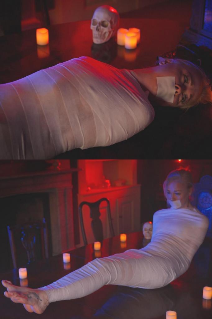 Policewoman Lucy Lauren Mummified by the Curse (VID0898) 女警露西·劳伦接到匿名举报，前往乡间一栋偏僻的老房子。她四处查看，发现没什么异常，于是敲门呼喊，然后进去调查。她发现一个奇怪的大厅，里面摆着一张大桌子，桌子上似乎摆放着某种祭坛，上面点着蜡烛，还有一本奇怪的古书。等等，那些书页好像是空白的……她正读着，一个恐怖的身影突然从她身后升起，抓住她，把她拖向死亡！<br><br>她发现自己躺在桌子上，周围都是蜡烛，一个怪异的钟在她头顶滴答作响。她从头到脚都被裹成了木乃伊，只有赤裸的双脚和头部没有被绷带束缚。她的嘴里塞着什么东西，被紧紧地贴在微孔泡沫胶带上，无法发出哭喊声。露西中了诅咒，变成了木乃伊，很快，诅咒就会永远地吞噬她！WPC Lucy Lauren has been called to a remote old house in the countryside by an anonymous tip-off. She walks around and inspects the place, can't see much so she knocks and calls out, then enters to investigate. She finds a strange hall with a huge table and what looks like some sort of altar set up with candles and a strange old book. Hang on, those pages seem to be blank... as she reads a ghastly figure rises behind her and grabs hold of her, dragging her off to her doom!<br><br>She finds herself on the table surrounded by candles, a weird clock ticking away time at her head. Mummified from head to foot, only her bare feet and her head are left unconfined by the bandages. Her cries are stopped by something filling her mouth and tight microfoam tape holding it in place. Lucy has been mummified by the curse, and soon the curse will claim her forever!