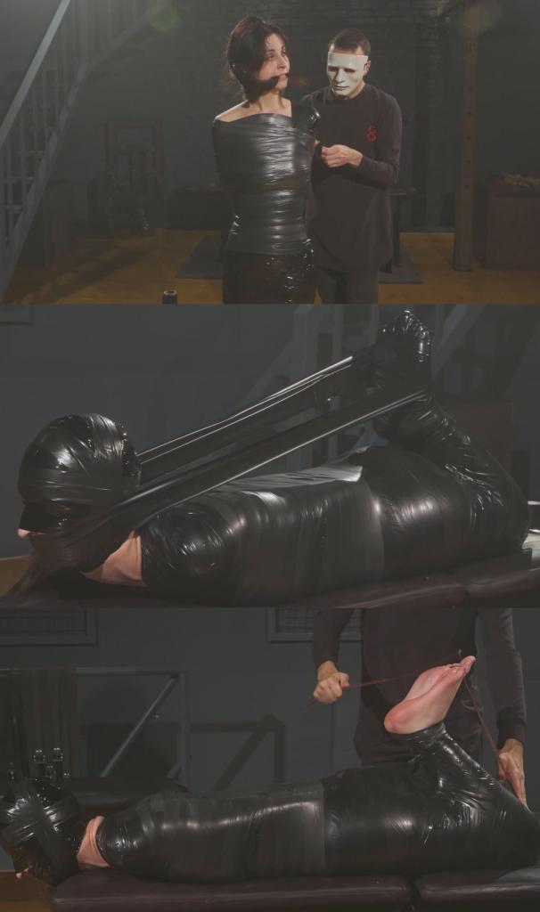 Antonia - Mummified in PVC Tape Hogtie 在这段视频中，安东尼娅被完全包裹成木乃伊——而且不是简单的茧状包裹，而是呈捆绑姿势。<br><br>视频展示了在安东尼娅身上制作木乃伊茧的整个过程。首先，我让她站立着，用保鲜膜包裹她。然后，我一层一层地用PVC胶带紧紧地缠绕在保鲜膜上。在这个阶段，我没有包裹她的头部和小腿，因为捆绑的姿势还需要稍后再做。<br><br>当她的身体被紧紧包裹后，我让赤脚的安东尼娅面朝下趴在长凳上，弯曲她的膝盖，继续缠绕，直到胶带下形成捆绑的形状。只有她的头部和脚部露在外面——但这种情况不会持续太久。<br><br>我用乳胶胶带完全包裹住她的头部，只留下鼻子的小开口供呼吸。头部被封住后，我转而缠绕她的双脚，也用PVC胶带固定，直到安东尼娅完全被捆成木乃伊状——除了脖子，为了安全起见，我没有缠绕脖子。<br><br>我短暂地用胶带将她的头和腿连接起来，使捆绑更加牢固。在那一瞬间，安东尼娅真切地感受到了彻底的无助。<br><br>之后，我剪断并解开了连接她头和腿的胶带，解开了她赤裸的双脚，这时她的脚已经汗湿了。我把她的大脚趾绑在一起，拉着脚趾把她的脚向后拉，然后轻轻地用棍子抽打她脆弱的脚底。<br><br>最后，我转身离开，留下被捆绑得动弹不得的安东尼娅独自一人待在我的地牢里。<br><br>尽情享受吧！In this clip, Antonia is fully mummified for a while - and not just in a straight cocoon, but in a hogtie position.<br><br>The video shows the entire process of creating the mummy cocoon on Antonia's body. First, I wrap her in stretch film while she is standing. Then I add tight PVC tape over it, layer by layer. At this stage, I leave her head and lower legs unwrapped, because the hogtie position still has to be built later.<br><br>Once her body is tightly wrapped, I place barefoot Antonia face down on the bench, bend her legs at the knees, and continue wrapping until the hogtie shape is formed under the tape. Only her head and feet remain exposed - but not for long.<br><br>I wrap her head completely with latex tape, leaving only small openings for breathing through the nose. After the head is sealed, I move to her feet and wrap them with PVC tape as well, stopping only when Antonia is fully mummified - except for the neck, which I leave unwrapped for safety.<br><br>For a short moment, I also connect her head back toward her legs with tape, creating an even stricter hogtie tension. In those moments, Antonia truly feels the depth of total helplessness.<br><br>After that, I cut and remove the tape connecting her head and legs, free her bare feet from the wrap, and by then they are already sweaty. I tie her big toes together and pull her feet back by them, then give her a short bastinado bonus on the vulnerable soles.<br><br>Finally, I step away and leave hogtied, deprived Antonia alone in my dungeon.<br><br>Enjoy!