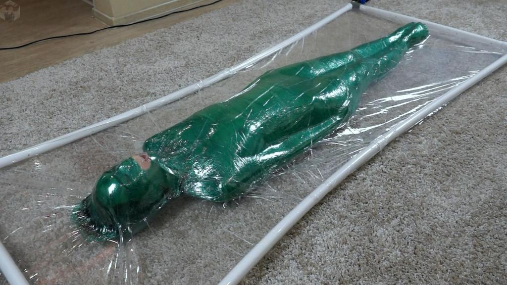 Green stretch mummifications cocoon in a transparent vacuum bed Oh, Sonya is a funny girl! What can not come into her mind. Look what her imagination has reached. The green stretch film looks so bright in the transparent vacuum bed. The girl got all wrapped up and lay down in the vacuum bed.