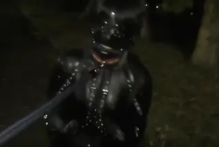 Woman in full latex catsuit is leashed by her master Woman in full latex catsuit is leashed by her master. She wears a full hood over the head, hand restraints, gag, and a massive black butt plug