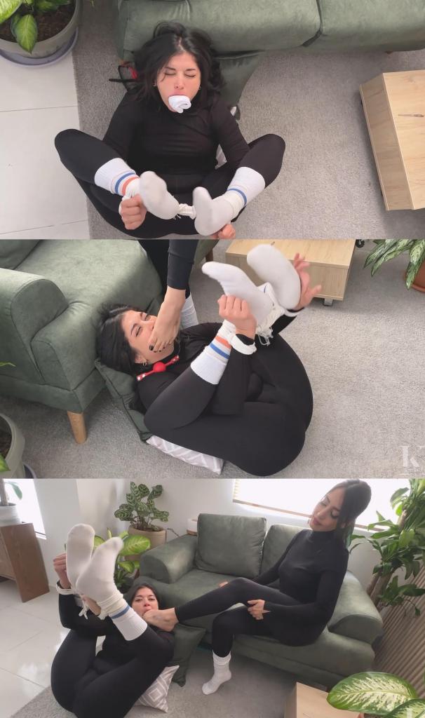 Simona Tied to be Foot Dominated by Mara 西蒙娜一身黑衣，高领毛衣配紧身裤，只有白色船袜和红色球形口塞格外显眼。她被独自留下，挣扎着，口水直流，直到玛拉过来，强迫她膜拜自己穿着袜子的脚，然后又让她光着脚。过了一会儿，玛拉让西蒙娜闻自己沾满口水的袜子，然后把袜子塞进她嘴里，让她再次挣扎。Simona is all in black, turtleneck, leggings, except for her white crew socks and her red ballgag, she's been left to struggle and drool until Mara comes to make her worship her socked foot, and then barefoot. After a while she makes Simona smell her socks drenched in saliva to then stuff it into her mouth and leave her to struggle again.